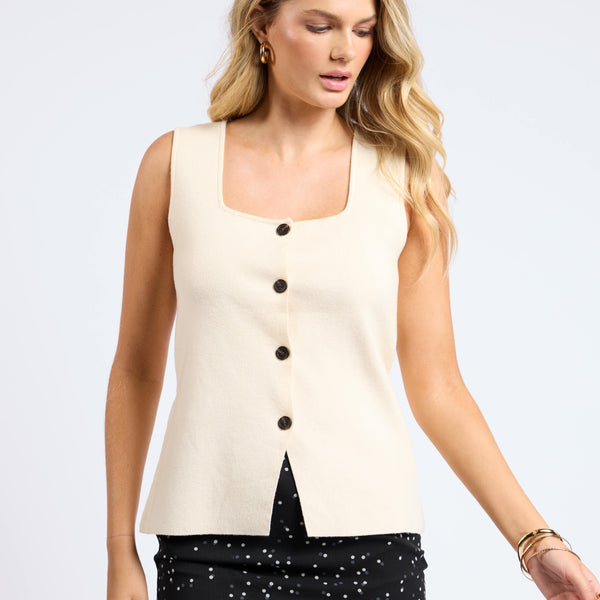 front view of the model wearing the myra button front knit vest. shows the square neckline. also shows the button closure, the wide straps and the slit at the bottom of the bottoms. its featured in this cream color. 