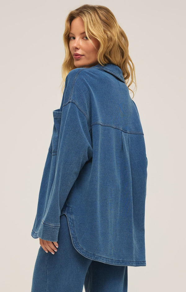 side/back view of the model wearing the all day knit denim jacket. shows the dropped shoulders. also shows the curved bottom hem, the collar and the oversized fit. 