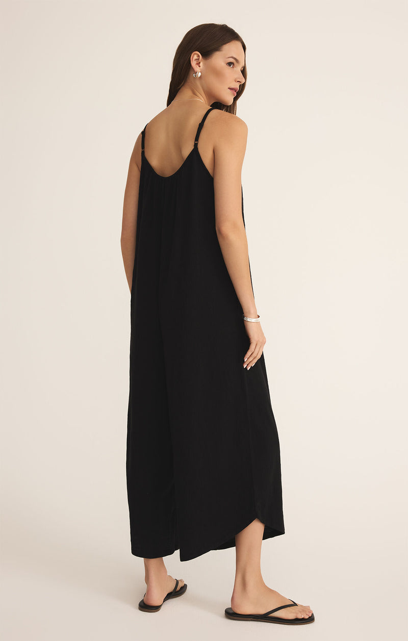 back view of the model wearing the selena textured flared jumpsuit. shows the the adjustable straps. also shows the flared bottoms, shows the bottom hem goes up alittle on the side, scoop neckline and pull on style. its in the color black. 